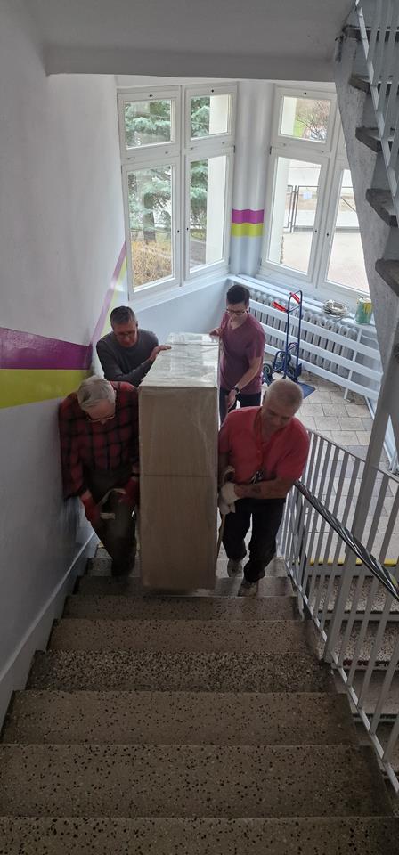 4 mężczyzn wnoszących szafki uczniowskie po schodach