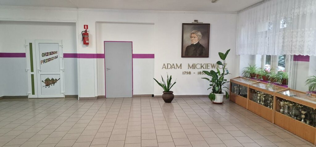 Zdjęcie przedstawiające korytarz szkolny. Na ścianie wisi portret Adama Mickiewicza