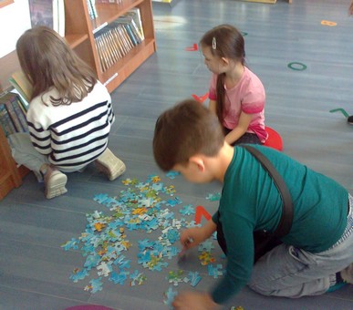Dzieci układają puzzle i oglądają książki na półkach