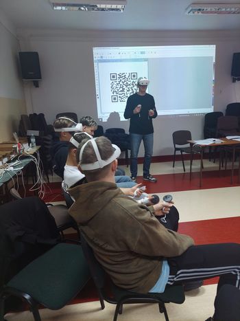 prowadzący zajęcia w goglach vr stoi a uczniowie w goglach siedzą