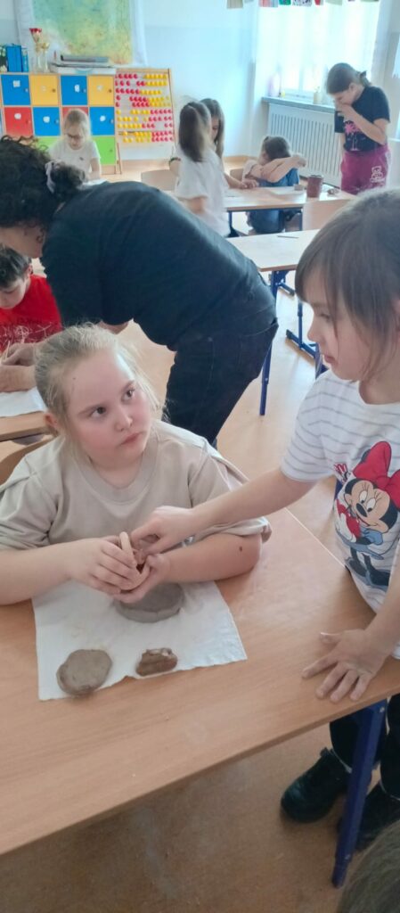 Uczennica pomaga drugiej przy ozdabianiu przedmiotu z gliny